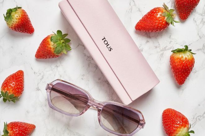 bodeg&oacute;n de uns &oacute;culos Tous com a sua bolsa e uns morangos em cima de uma bancada