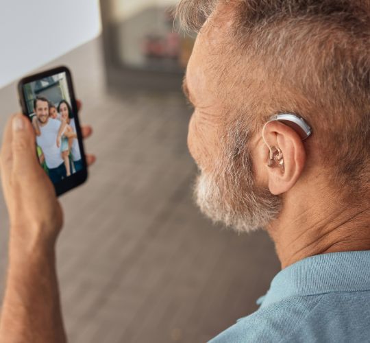 utilizador de aparelhos auditivos a olhar para um telem&oacute;vel