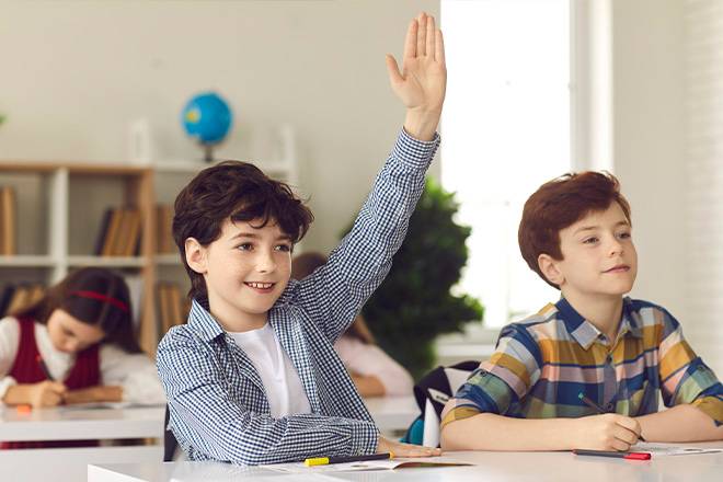 Criança numa sala de aula a levantar a mão